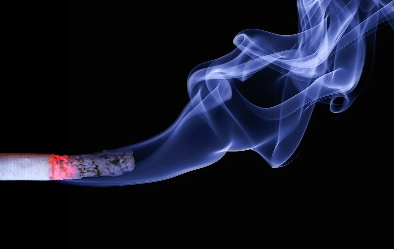 Burning cigarette with smoke trailing off ito
