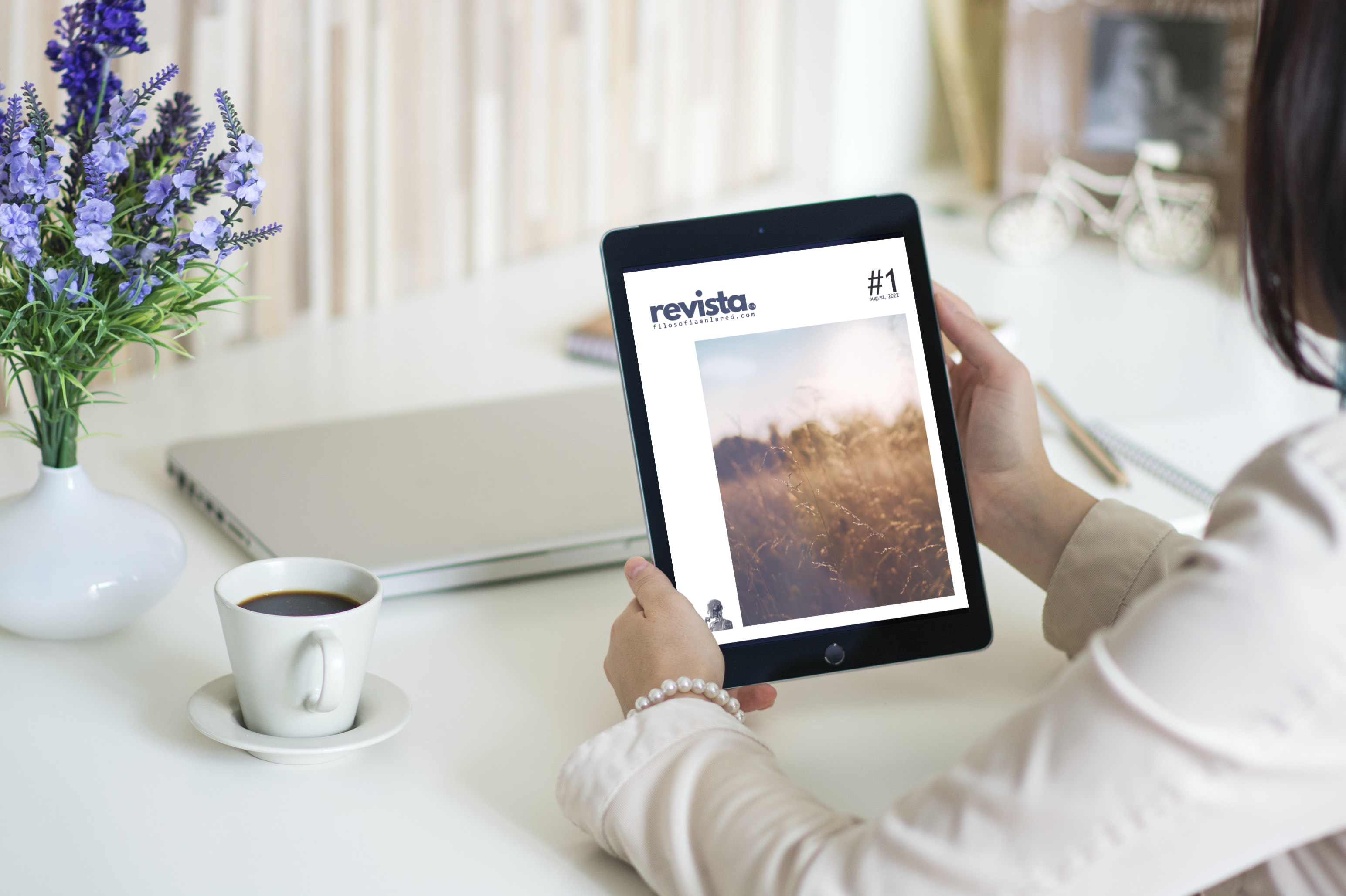 Person reading Revista on a tablet at a white desk with purple flowers on it