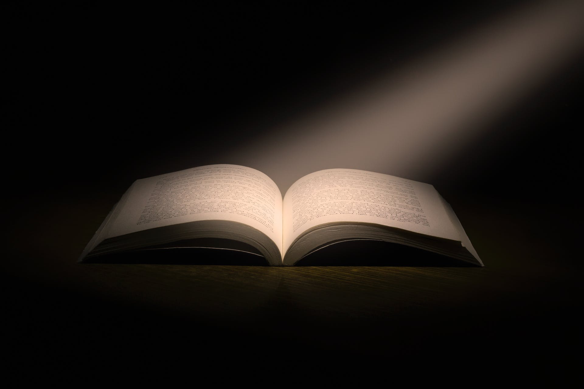 book lying open against a dark background with shaft of light illuminating the book