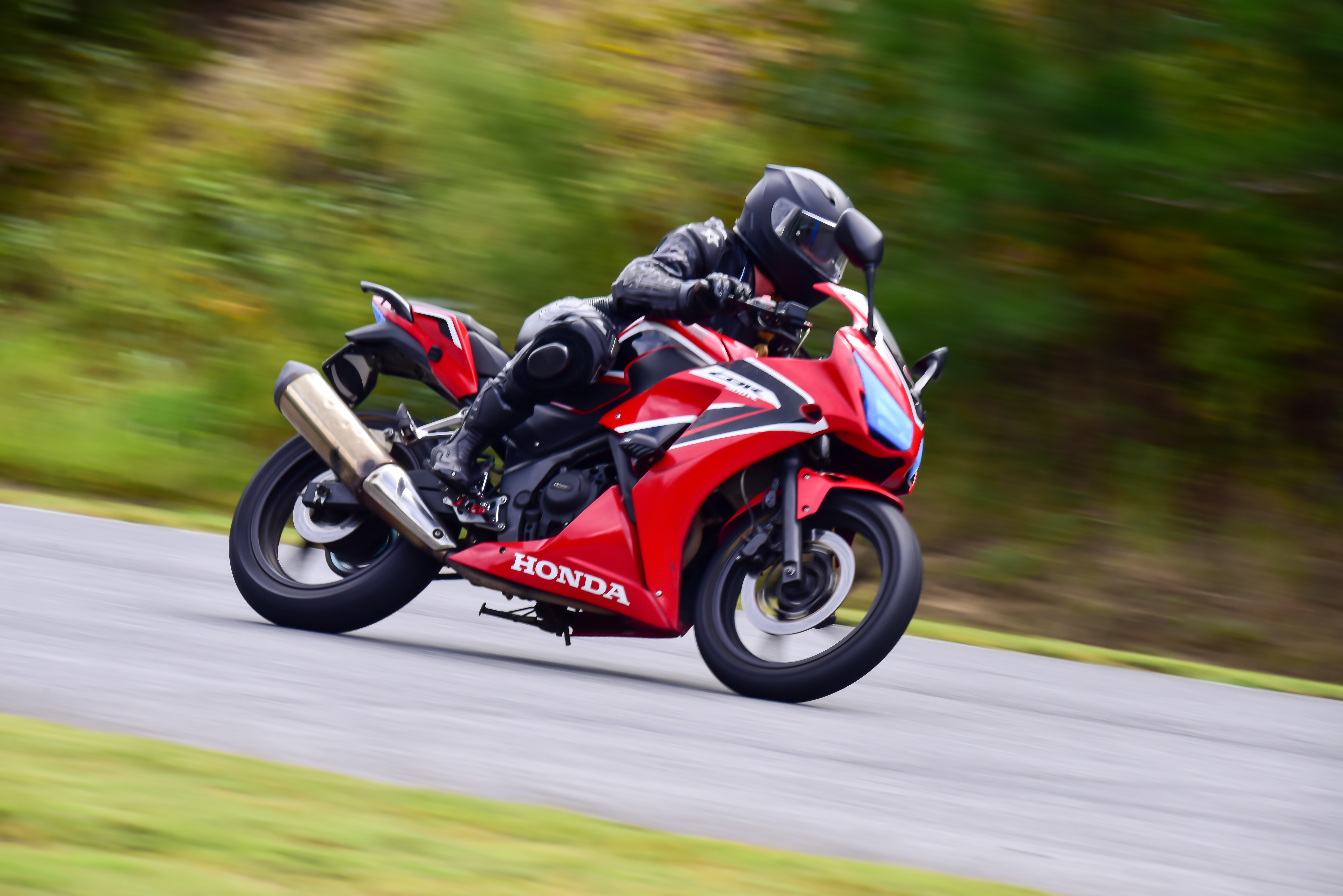 Person dressed in black protective gear on a red motorcycle with a blurry background.