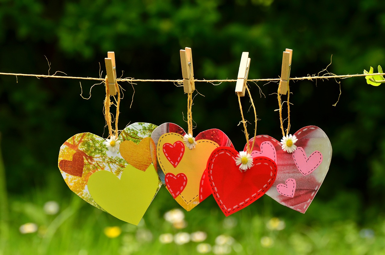 Cut out hearts made from collage paper hanging on a clothes line in front of a field of flowers.