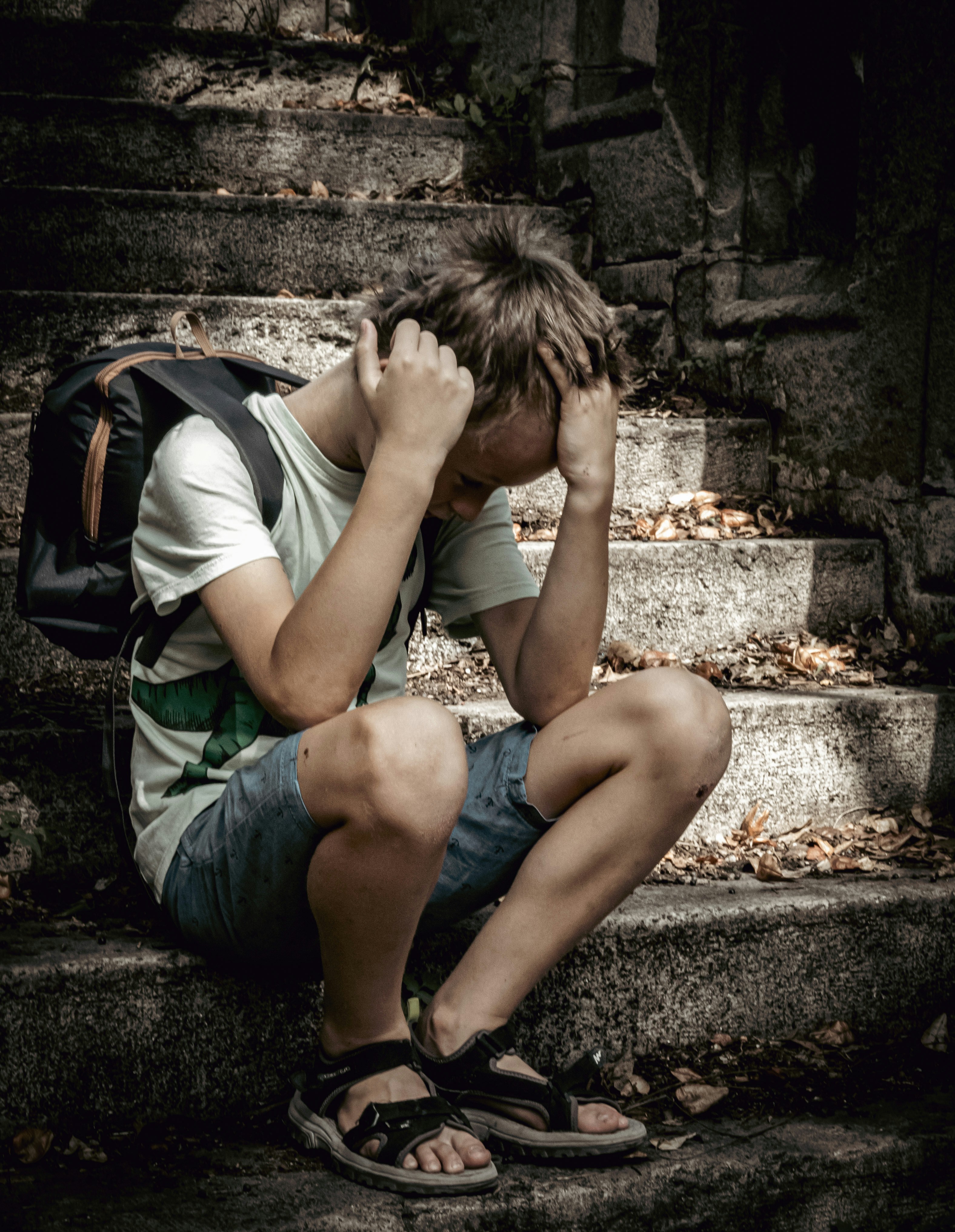 A boy sits on concrete stairs covered in leaves with his head in his hands