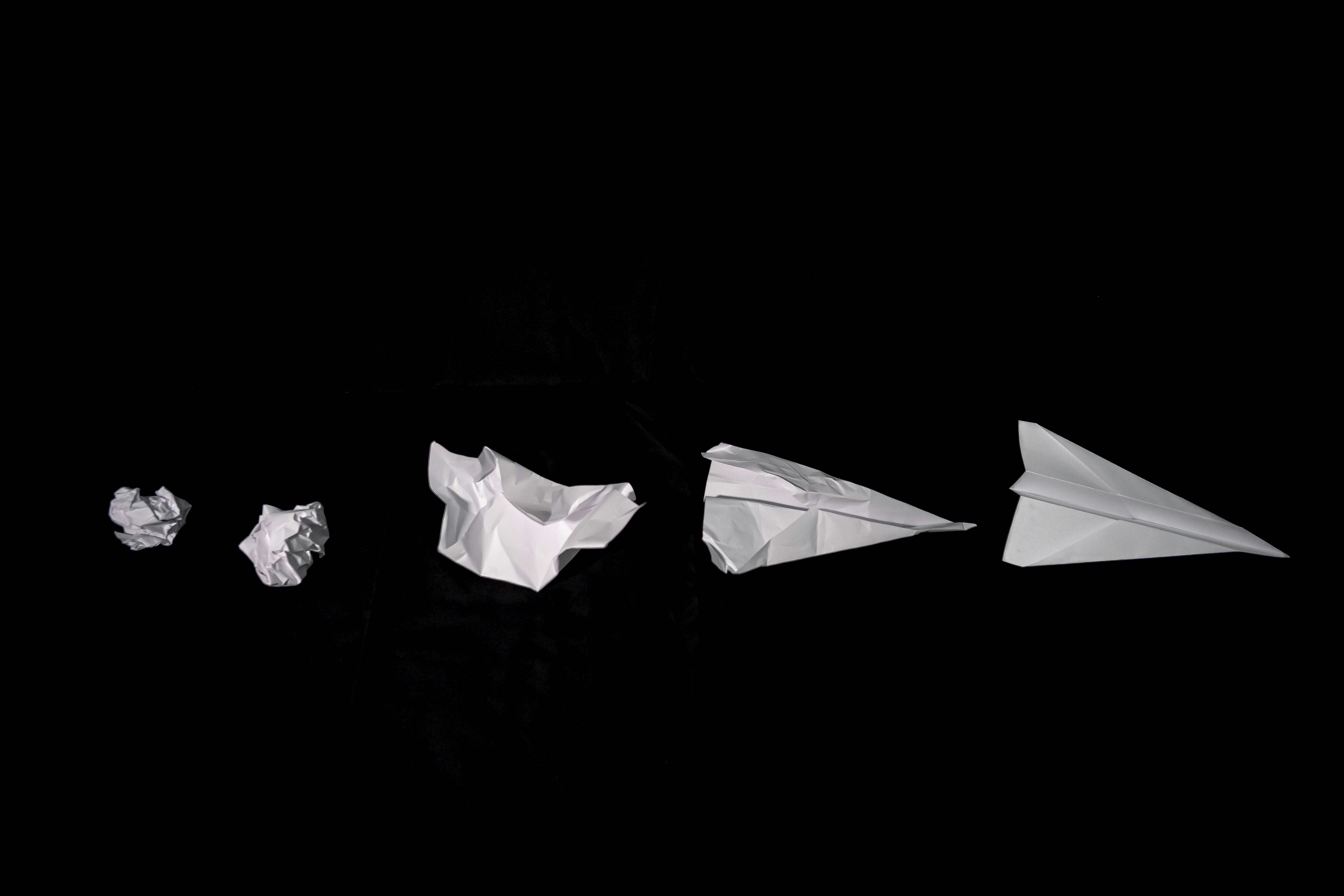 joshua-dixon-lRhedSIgeo0-unsplash A crumpled sheet of white paper folded into an origami airplane on a black background